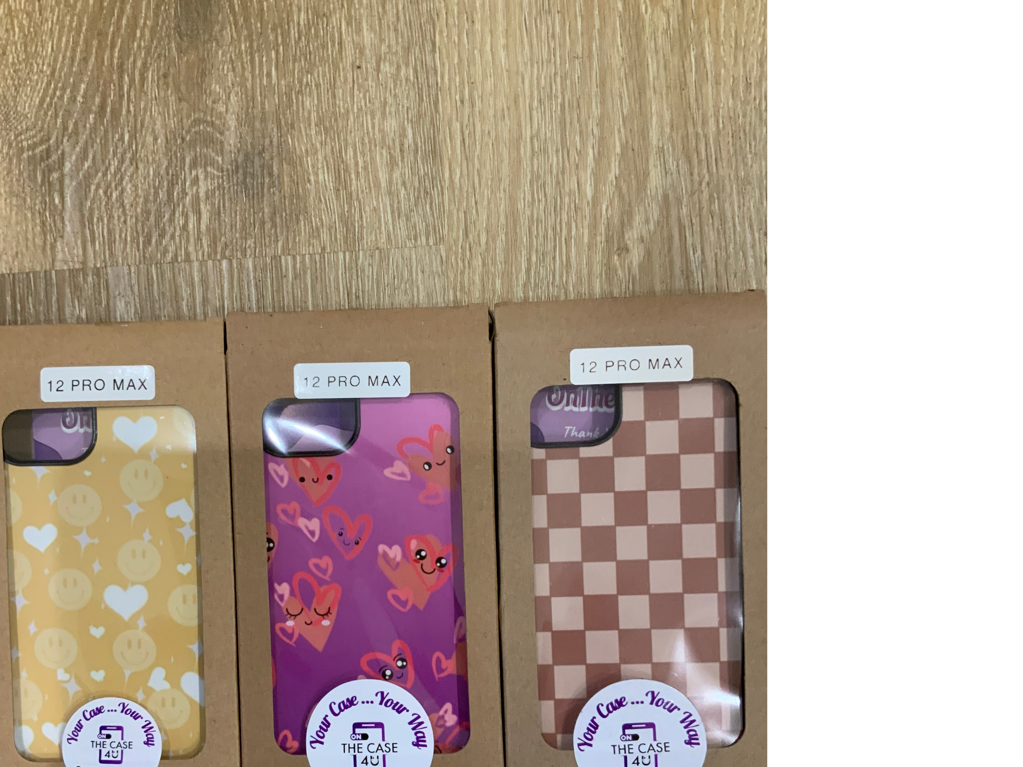 A set of four iPhone 12 Pro Max phone cases with various designs, including a checkered pattern and heart motifs, displayed in a clearance sale setting.